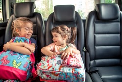 Children in the car go to school, happy, sweet faces of sisters, pupils of a kindergarten with school backpacks, sitting in the parental car