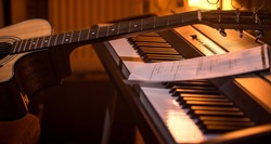 acoustic guitar stands on piano with notes, close-up, beautiful color background, music activity concept