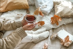 Cozy autumn at home, a woman with tea and a book resting. A cozy way of life . Body parts in the composition.