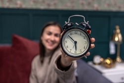 Black retro alarm clock in female hands on a blurred background.