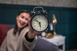 Black retro alarm clock in female hands on a blurred background.