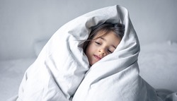 Sleepy little girl wrapped in a white blanket.