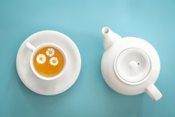 A cup of chamomile tea and a teapot on a blue background.