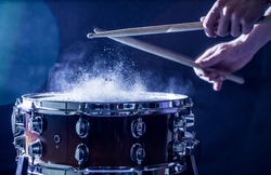 man plays musical percussion instrument with sticks closeup on a black background, a musical concept with the working drum, beautiful lighting on the stage