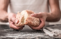 the preparation of bread, fresh bread in hands closeup on old wooden background, concept for baking