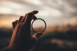 man's hand is holding an optical ring out of focus city