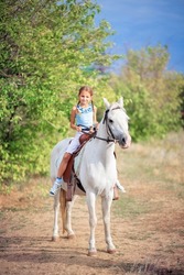 Schoolgirl girl rides a white pony. The child is riding a horse. Horse riding training for children. Controlling the horse with the reins