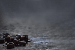 Group of rusty nuts and old screws from auto part pile on the dusty cement floor with selective focus and copy space. Background for mechanical or recycle concept. 