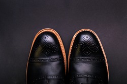 Black shoes with a brown sole on a black background

