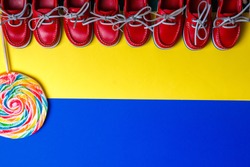 A lot of small red boat shoes near big multicolored lollipop on colored background.  Top view, copy space. Frame. group of child boat shoes.