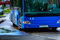 the blue bus is approaching the bus stop to pick up passengers