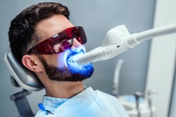 Close up view of man undergoing laser tooth whitening treatment to remove stains and discoloration.