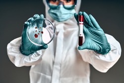 Unrecognizable female scientist with bacteriological protection suit examining a petri dish in the laboratory