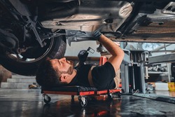 Male car mechanic worker working using wrench tool for repair, maintenance underneath car. Mechanic vehicle service checking under car in garage. Auto car repair service, maintenance concept.