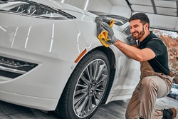 Man cleaning car and drying vehicle with microfiber cloth. Hand wipe down paint surface of shiny white car after polishing and ceramic coating. Car detailing and car wash concept. Selective fiocus.