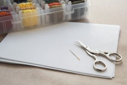 Aida white canvas, needle, needlework scissors and a box with multicolored embroidery threads, needlework and cross stitch concept