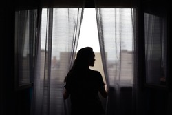 Silhouette of beautiful woman next to window with net curtains in backlight during the situation of confinement in Madrid due to the coronavirus, Covid-19.