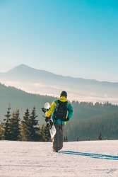 man walking by hill with snowboard mountains on background