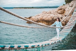 woman crossing suspension bridge sea on background summer time