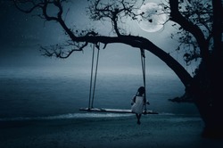 The little girl sits on the seaside swing on a full moon night.