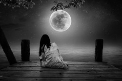 A black and white image, a woman sitting on a bridge on a full moon alone