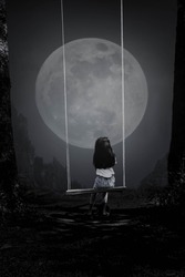 A black and white picture of a young woman riding a swing looking at the full moon in the lonely night