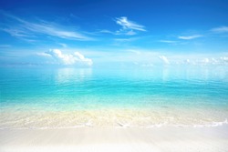 Beautiful sandy beach with white sand and rolling calm wave of turquoise ocean on Sunny day. White clouds in blue sky are reflected in water. Maldives, perfect scenery landscape, copy space.
