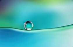 Beautiful clean bright drop of water on smooth surface in blue and turquoise colors, macro. Creative image of beauty of environment and nature.