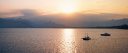 Amazing beautiful panoramic natural seascape with sunset with sunset in pink and gold tones. Evening sun hides behind mountains against the backdrop of Mediterranean Sea with ships.