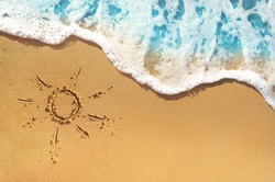 Soft waves with foam blue ocean sea on a golden sunny sandy beach in resort on summer vacation rest. The symbol of the sun drawing on the sand. Background close up