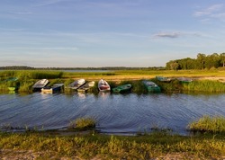 Beautiful, calm, shallow shore of the lake in the summer evening at sunset. Fishing boats are located along the edge of the boat dock. Lake Burtnieks, Latvia