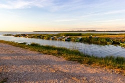 Beautiful, calm shore of the lake in the summer evening at sunset. Fishing boats are located along the edge of the boat dock. Lake Burtnieks, Latvia