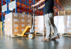 warehouse worker is working with hand pallet truck or pallet jack and shipments in distribution warehouse.