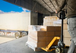 Cargo shipment loading for truck.Worker courier unloading cargo pallet shipment goods, package box, his using hand pallet jack load into a truck, Road freight transport. Industrial warehouseing.