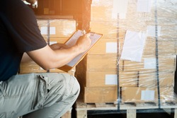 Warehouse worker holding clipboard writing on checklist for delivering shipment goods. Package boxes, Cargo shipment export, Industry warehouse shipping logistics and transport.
