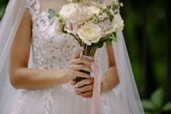 the bride holds a wedding bouquet of flowers at the ceremony. the bride holds a bouquet in hands. The bride is holding a wedding bouquet, wedding dress, wedding details.