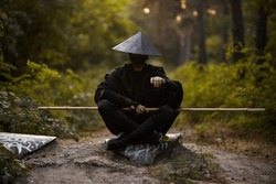 Surrealism theme: a man in a hannya mask, black kimono, black hat with a bamboo stick in his hands in the forest. Surreal image of a man in a hannya half mask, kimono. Surreal samurai, surreal ninja