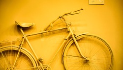 close up of bicycle as decoration on the wall. old painted bicycle attached to the wall in art office toned to yellow golden color. vintage bicycle on decorative color wall