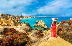 Landscape with unknown tourist girl is looking to the amazing view of spectacular rock formations, with caves, grottoes and sea arches in Lagos, Algarve, Portugal