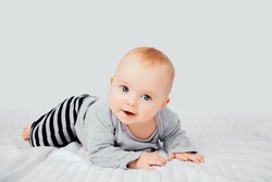 Seven month old baby child sitting on bed. Cute smiling little infant girl on white soft blanket. Charming blue eyed baby. Copy space.