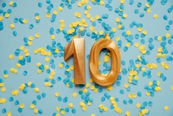 Number 10 ten golden celebration birthday candle on yellow and blue confetti Background. Ten years birthday. concept of celebrating birthday, anniversary, important date, holiday