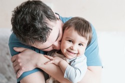 Close-up portrait of happy young father hugging and kissing his sweet adorable child. Indoors shot, concept image