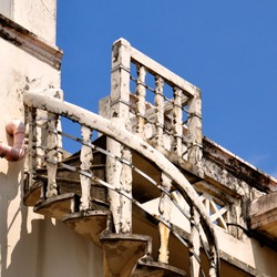 Rustic external white spiral staircase, with ornate column balustrades, leading to a roof top space