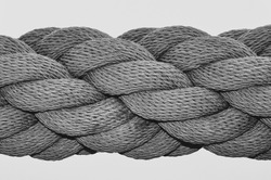 A black and white close up image of a thick industrial rope, with many rope lengths coiled together in a spiral.