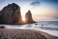 Sunset at Ursa Beach Sea stack, Portugal. Atlantic Ocean Foamy waves rolling to sandy beach. Holiday vacation landscape scene