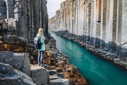 Woman hiker with backpack enjoying Studlagil Canyon. Unique Jokulsa basalt colums and A Bru river. Spectacular outdoor scene of Iceland, Europe. Beauty of nature concept background
