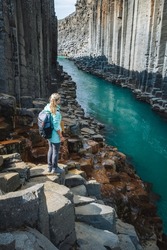 Woman hiker with backpack enjoying Studlagil Canyon. Unique Jokulsa basalt colums and A Bru river. Spectacular outdoor scene of Iceland, Europe. Beauty of nature concept background