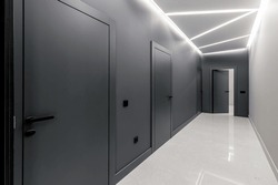 Simple clean newly built generic modern new real estate block of flats interior, long black corridor with black doors, perspective. New bought apartment, new home, hallway abstract concept