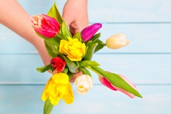 Romantic concept. Close up of colorful tulip flowers in female hands against light blue wooden background. Colorful and fresh flower bouquet. Mothersday concept.