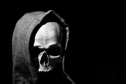 Human skull in hood close up on black background.